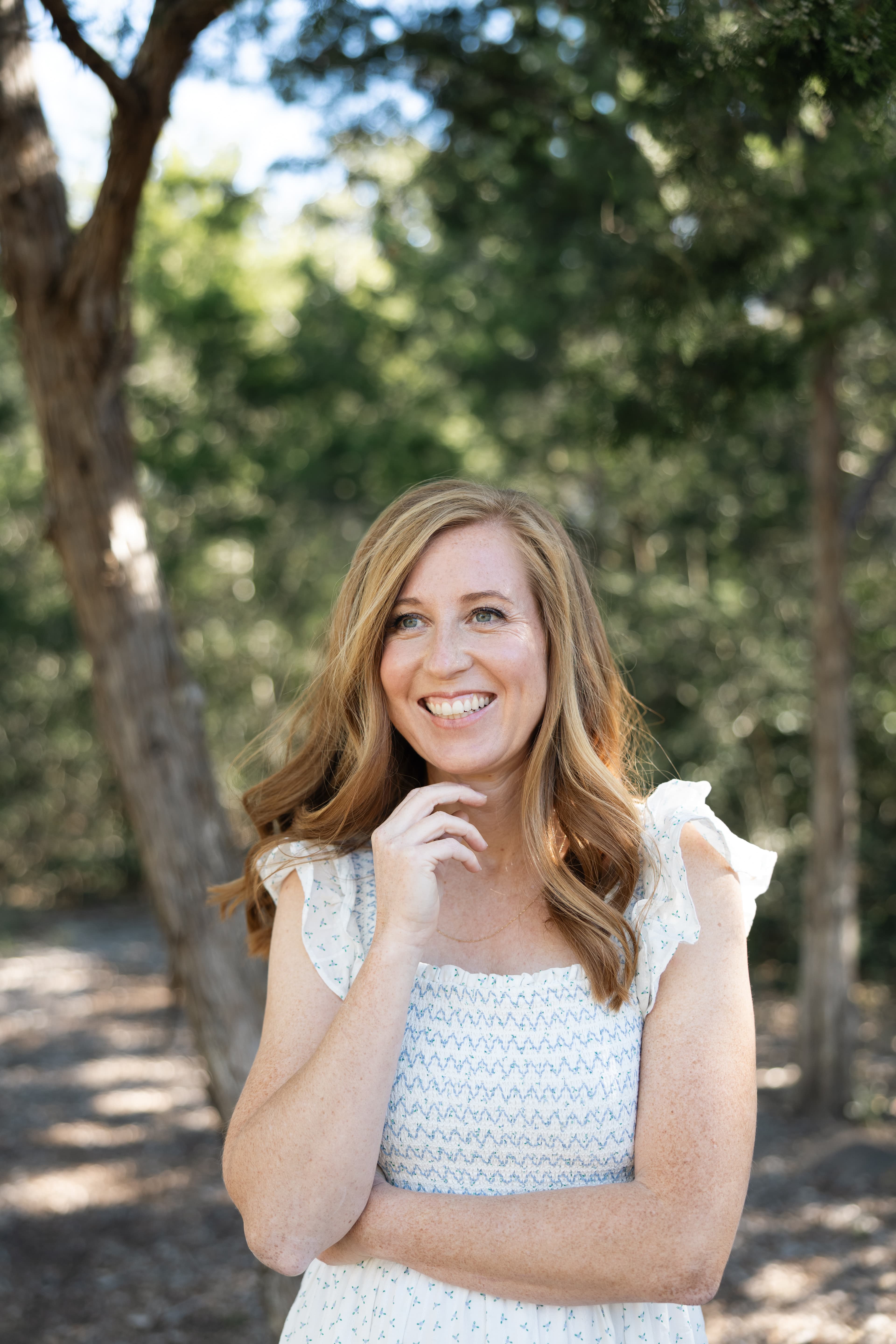 Katie smiling warmly outdoors among trees